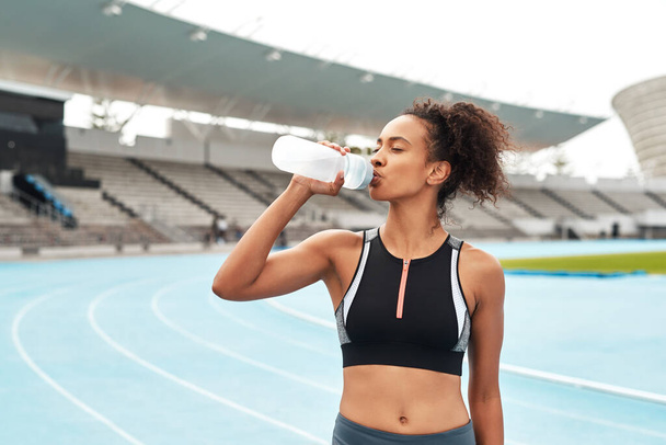 Fitness, running and woman on track drinking from bottle at stadium, relax during marathon training or exercise. Workout time, health and wellness, healthy female sports runner at area with water - Photo, Image