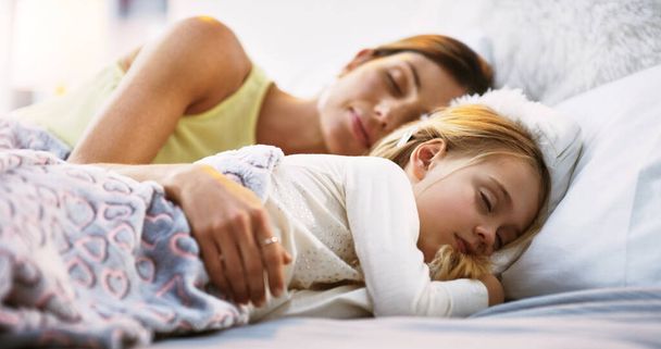 Χαλαρώστε, κοιμηθείτε και μια μητέρα στο κρεβάτι με την κόρη της το πρωί, ενώ ονειρεύονται στο σπίτι τους μαζί. Οικογένεια, παιδιά και μια γυναίκα κοιμούνται στην κρεβατοκάμαρα με το μικρό θηλυκό παιδί της για ειρηνική ανάπαυση. - Φωτογραφία, εικόνα
