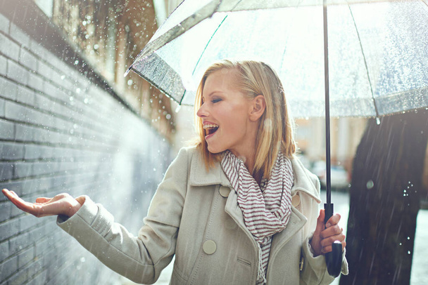 Lachen, vrolijke vrouw en regen voelend water in de stad met paraplu, vrijheid en geluk. Winterweer, regen en stedelijke straat met een jonge vrouw op een trottoir en vakantie buiten. - Foto, afbeelding