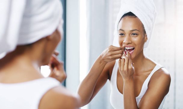女性は、歯の健康のための製品とバスルーム、鏡や口腔衛生、朝のルーチンで歯をフロスします。身だしなみやセルフケアで家の中で女性の人,開花と健康ときれいな口. - 写真・画像