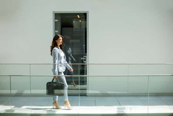 Hübsche junge Geschäftsfrau läuft mit Aktentasche im Büroflur - Foto, Bild