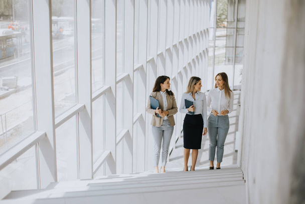 Drie leuke jonge zakenvrouwen lopen op de trap in de hal van het kantoor - Foto, afbeelding
