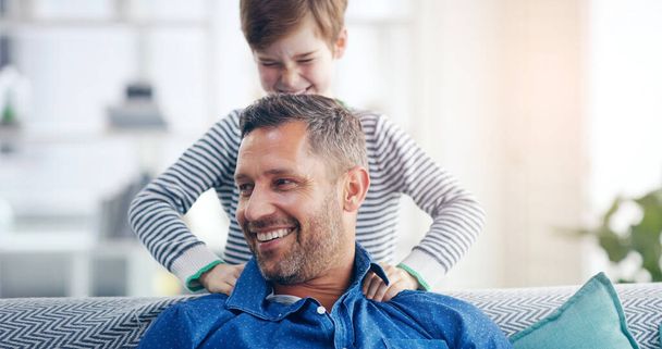 Love, father and son happy smile in living room of their home with lens flare. Happiness or caring, family and male parent with child playing spending quality time or bonding together on couch. - Photo, Image