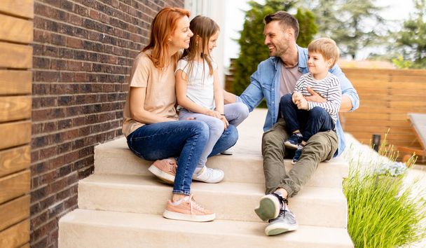 Family with a mother, father son and daughter sitting outside on  steps of a front porch of a brick house - Foto, Imagen
