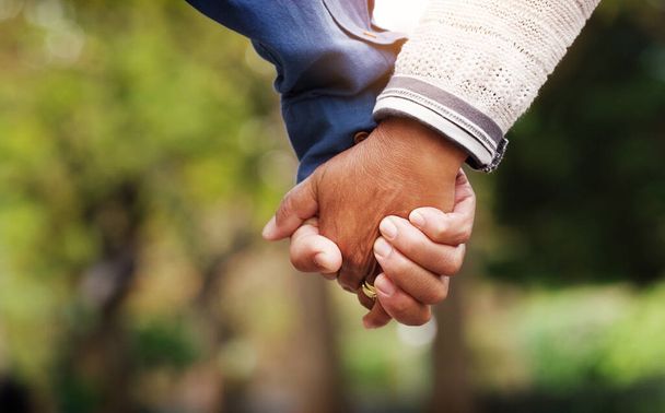 Liefde, close-up senior koppel hand in hand en in een park natuur achtergrond. Ondersteuning of verzorging, hechting of kwaliteitstijd en getrouwde bejaarden samen buiten in een tuin of in een groene omgeving - Foto, afbeelding