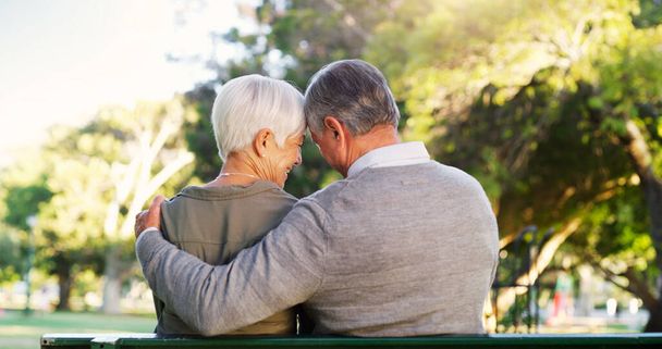 Senior couple, hug and bench outdoor in a park with love, care and support in marriage. A elderly man and happy woman in nature with a smile for quality time, healthy retirement and freedom to relax. - Photo, Image