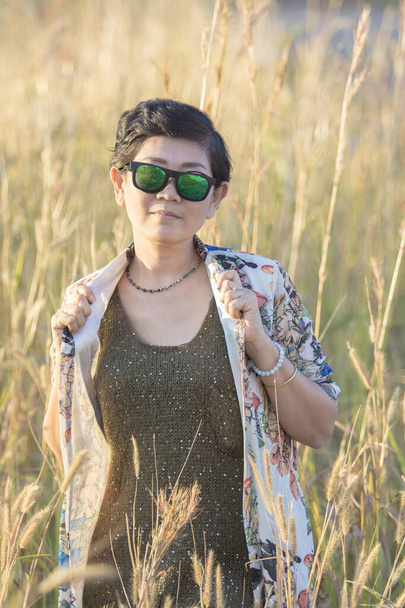 krásná asijská žena nosí sluneční brýle stojící v trávě pole  - Fotografie, Obrázek