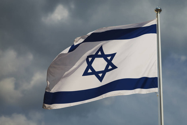 Heiluttaa Israelin värikästä lippua pilvistä taivasta vasten. Erittäin yksityiskohtainen kangas rakenne. Sinivalkoinen tähti pilviä vastaan. Jerusalemin Israelin pääkaupunki. Itsenäisyyspäivä
 - Valokuva, kuva