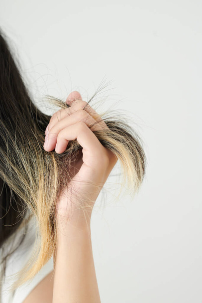 Κοντινό πλάνο εικόνα της γυναίκας που δείχνει βαμμένα ξηρά μπερδεμένα μαλλιά της - Φωτογραφία, εικόνα