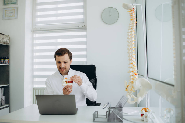 un médico vertebrologista trabaja en una cámara detrás de una computadora portátil. - Foto, Imagen