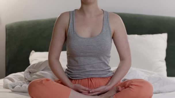 Close-up van jonge blanke vrouw mediteert zittend op bed. Een Jib shot. Avond yoga voor het slapen gaan. Rust en ontspanning. - Video