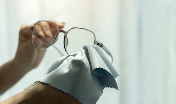 Kız okuma gözlüklerinin lenslerini arka planda elle temizliyor. Temizlik ve gözlük bakımı konsepti. - Fotoğraf, Görsel
