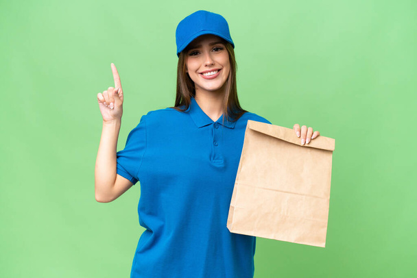 Jovem bela mulher caucasiana levando um saco de comida takeaway sobre fundo isolado mostrando e levantando um dedo em sinal do melhor - Foto, Imagem