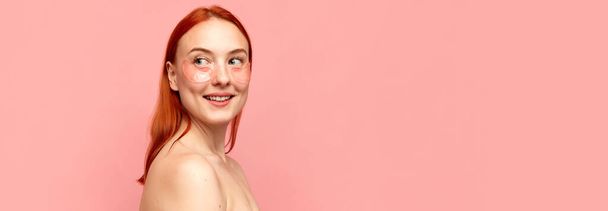 Banner with portrait of young adorable girl with bare shoulders using eye patches for skin refreshing over pink background. Concept of beauty, natural make-up, skin care, healthy look, cosmetology - Photo, Image