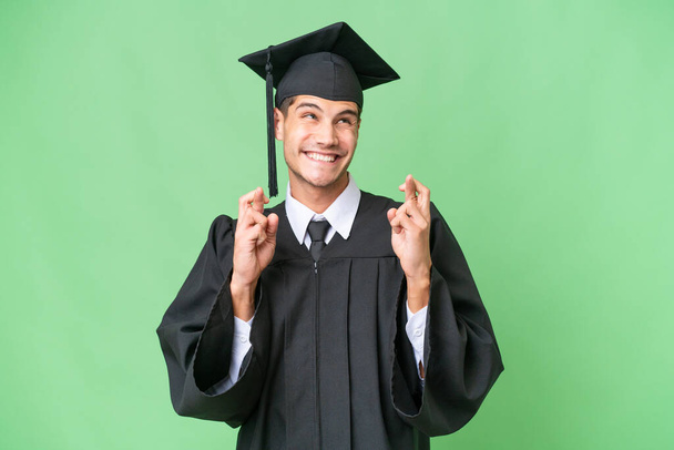 Mladá univerzita absolvent běloch muž přes izolované pozadí s prsty křížení - Fotografie, Obrázek
