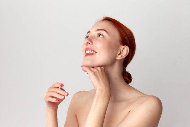 Close up shot of happy, adorable girl with perfect skin and red hair doing neck massage over white studio background. Beauty, spa, cosmetology, skin care, emotion concept. Model with well-kept skin - Photo, Image