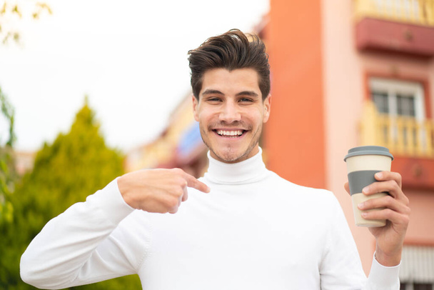 Jeune homme caucasien tenant un café à emporter à l'extérieur avec expression faciale surprise - Photo, image