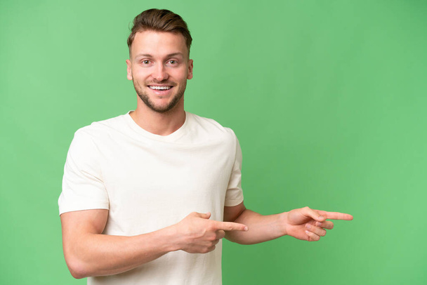 Young blonde caucasian man over isolated background surprised and pointing side - Photo, Image