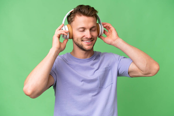 Young blonde caucasian man over isolated background listening music and singing - Foto, Imagem