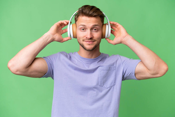 Молода блондинка білий чоловік над ізольованим фоном слухає музику
 - Фото, зображення