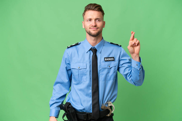 Mladý policista přes izolované pozadí s prsty kříž a přeje to nejlepší - Fotografie, Obrázek