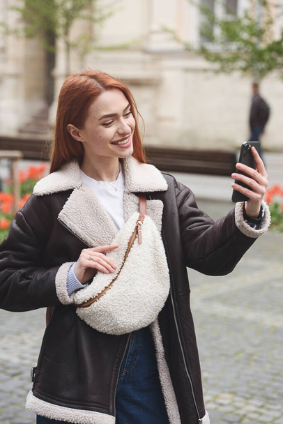 gelukkig vrouw communiceert met vrienden via video link buiten op een oude stad straat. - Foto, afbeelding