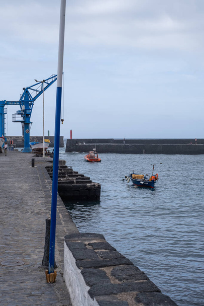Blue antique crane from a pier. Jetty and ocean with some boats in the background. Puerto de la Cruz, Tenerife, Canary Islands, Spain. - Foto, Imagen
