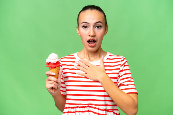 Mujer árabe joven con un helado de corneta sobre fondo aislado sorprendida y sorprendida mientras mira a la derecha - Foto, Imagen