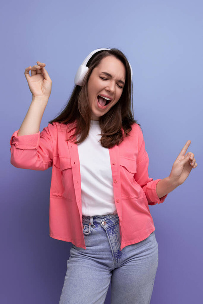 enjoying brunette young woman with dark hair below her shoulders in a shirt and jeans with wireless headphones. - Photo, Image