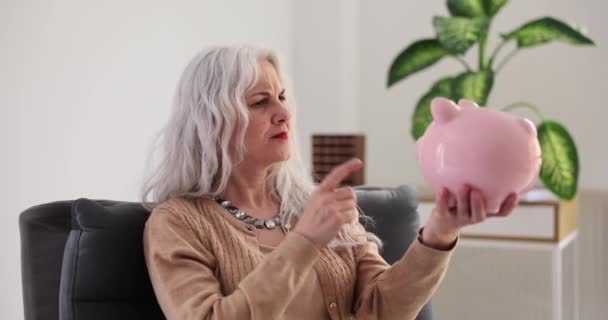 Mujer disgustada enojada infeliz sosteniendo alcancía. Reforma de las pensiones y pequeña pensión en efectivo - Imágenes, Vídeo