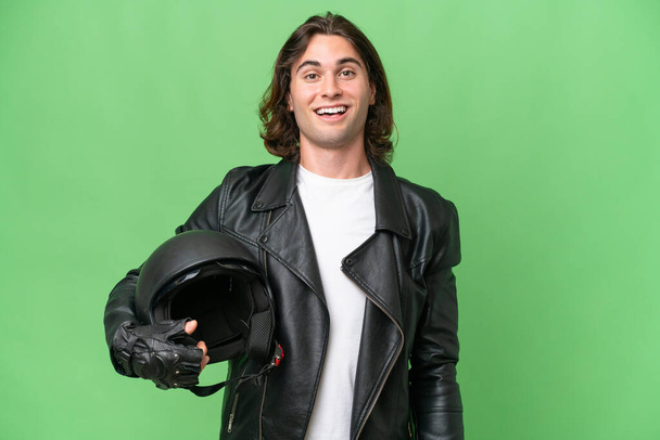 Jeune homme beau avec un casque de moto isolé sur fond de chroma verte avec expression faciale surprise - Photo, image