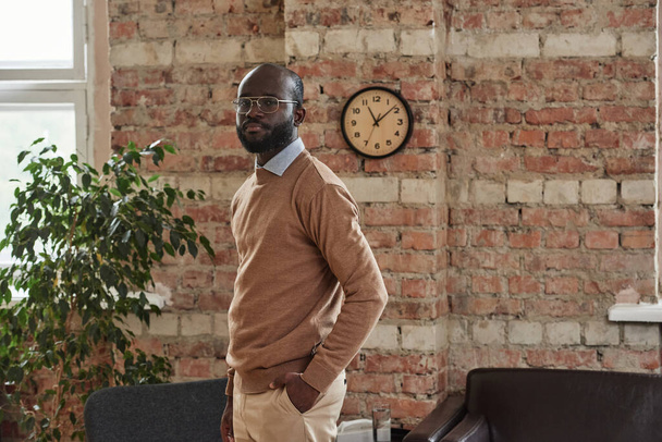 Portrait of confident bald African American entrepreneur with beard standing against brick wall in modern office - Photo, image