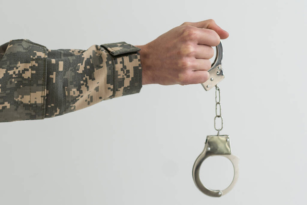 Ein Militärmann in Handschellen hält vor dunklem Hintergrund ein Armeeabzeichen in der Hand, selektiv fokussiert. Konzept: Kriegsverbrecher, Kriegsgefangener, Tribunal für Deserteure, Vaterlandsverräter. - Foto, Bild