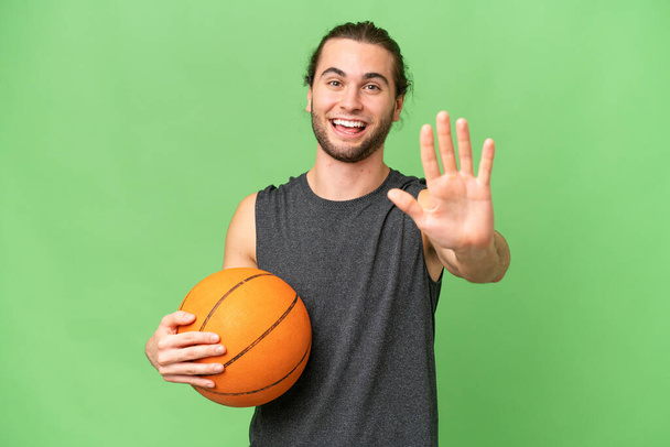 Jeune joueur de basket-ball homme sur fond isolé comptant cinq avec les doigts - Photo, image