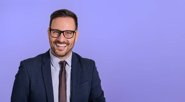 Portrait of handsome cheerful male professional chief wearing eyeglasses and elegant suit looking at camera. Happy businessman smiling cheerfully and posing against isolated blue background - Photo, Image