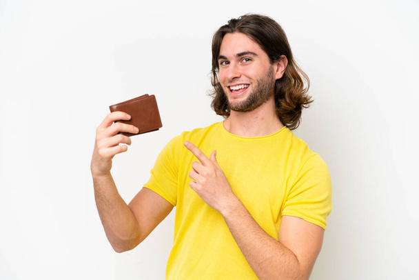 młody przystojny mężczyzna trzymając portfel odizolowany na białym tle i wskazując go - Zdjęcie, obraz