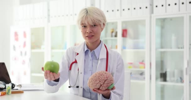 Tohtori pitää kädessään vihreää omenaa ja anatomista aivomallia. Terveelliset elintarvikkeet aivoille - Materiaali, video