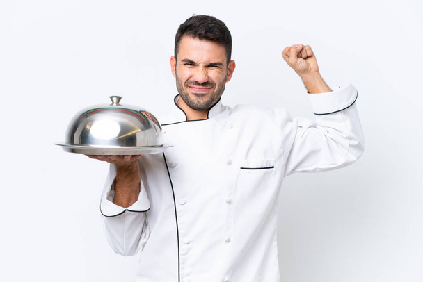 Joven chef con bandeja aislada sobre fondo blanco haciendo un gesto fuerte - Foto, imagen