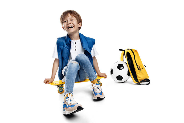 Cute laughing blonde boy sitting on yellow skateboard on white background. Back to School - Foto, afbeelding
