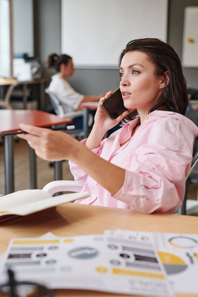 Modern young businesswoman in blouse discussing project by phone while working in coworking space - Fotoğraf, Görsel