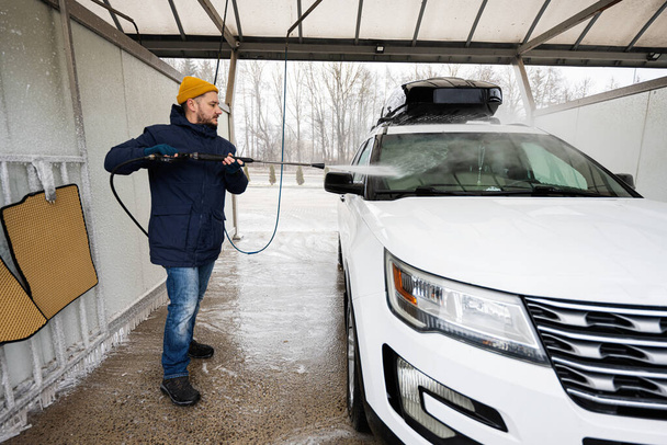 Man washing high pressure water american SUV car with roof rack at self service wash in cold weather. - Foto, Imagen