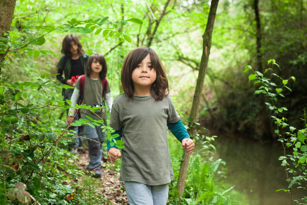 Tři sourozenci procházející se a prozkoumávající les u potoka. V popředí vede cestu nejmladší sourozenec. - Fotografie, Obrázek