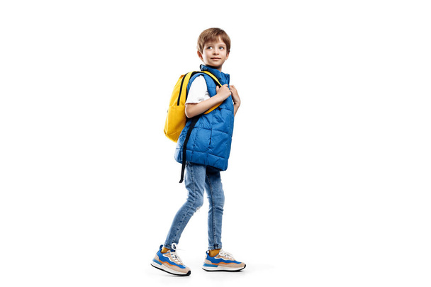 Full lengh image of a little boy with backpack walking over white background. Back to School. Looking away - 写真・画像