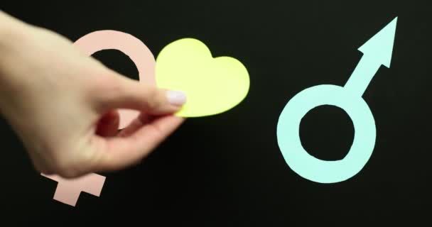 A női kéz nő és férfi szimbólumok közé helyezi a szívet. Szerelem férfi és nő között - Felvétel, videó