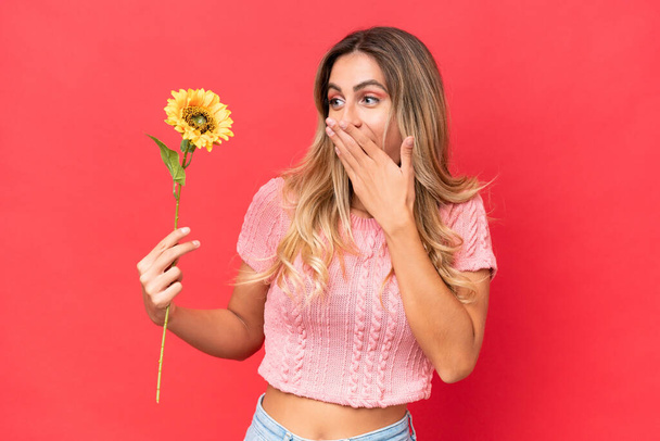 Mladý pěkný Uruguayan žena držení slunečnice izolované na pozadí s překvapením a šokovaný výraz obličeje - Fotografie, Obrázek