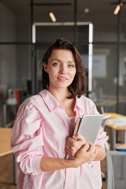 Portrait of smiling attractive young Caucasian businesswoman standing with tablet and diary in office - Foto, afbeelding