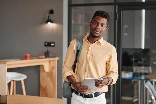 Portrait of content modern African-American student standing with digital tablet and satchel in cafe - Foto, imagen