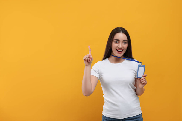 Smiling woman holding vip pass badge and pointing at something on orange background. Space for text - Φωτογραφία, εικόνα