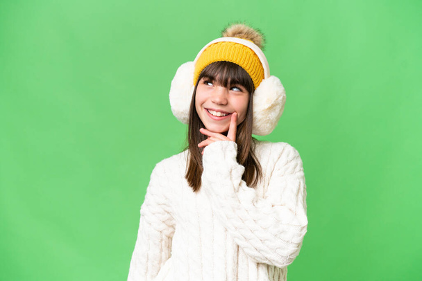 Μικρό καυκάσιο κορίτσι που φοράει χειμωνιάτικες μανσέτες σε απομονωμένο φόντο σκεπτόμενο μια ιδέα ενώ κοιτάζει ψηλά - Φωτογραφία, εικόνα