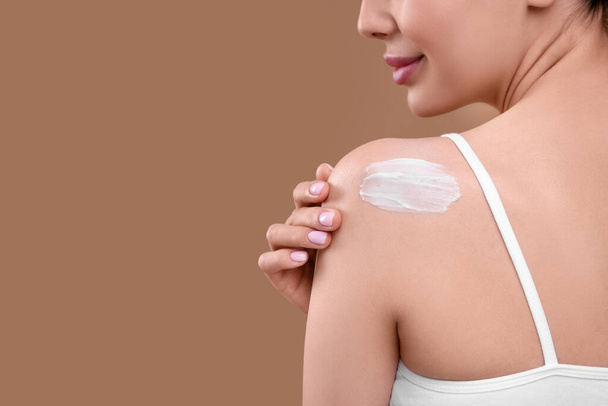 Woman with smear of body cream on her shoulder against light brown background, closeup. Space for text - Foto, Imagem